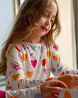 A girl wearing our Albi Long Sleeve Pyjama, smiling softly as she plays and explores colorful cards.
