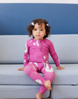 A calm little girl sitting on the couch while wearing our Arqam Smart Baby Pyjama, featuring playful Arabic numbers in a fun magenta design.