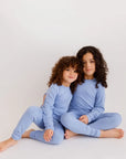 Two siblings sitting together in our Bahry Long Sleeve Kids Pyjamas, showcasing the cozy softness and calming blue tone of our bamboo fabric.
