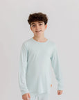 A young boy wearing the **Reef Pyjama** from the **Ramady & Reef Bundle**, a light seafoam-blue bamboo set designed for breathability, softness, and effortless comfort.