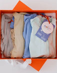 The **Grow with Nohm: Gift Set** displayed in an orange box, featuring four neatly folded baby pyjamas in soft neutral and pastel shades, each with a zipper design and Nohm tag.
