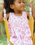 A joyful girl swinging outdoors while wearing our Yasmine Dress, blooming with pink jasmine flowers that capture playful elegance.