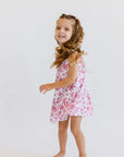 A joyful girl twirling in our Yasmine Dress, featuring a soft pink jasmine flower pattern that captures playful elegance.