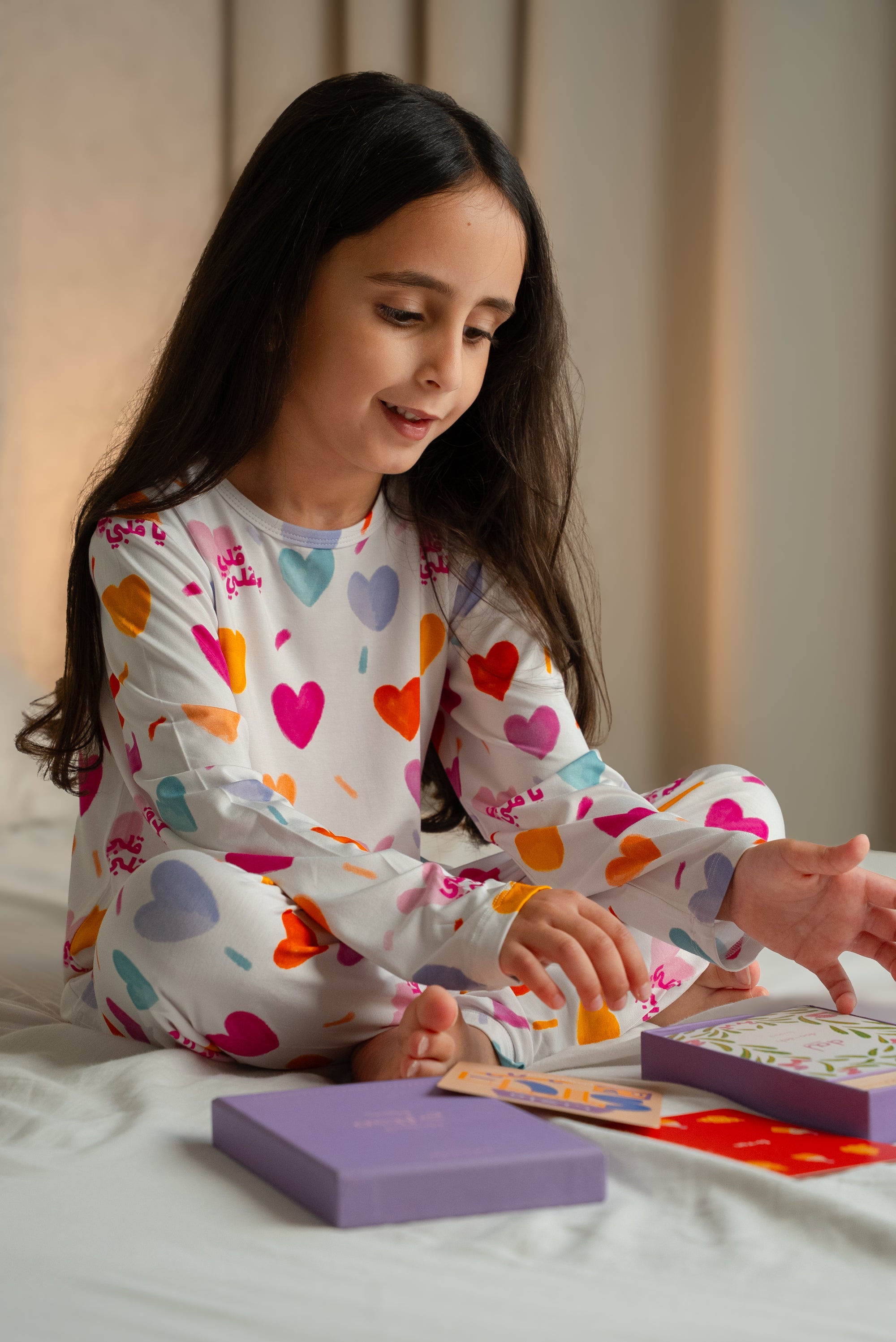 A girl wearing our Albi Long Sleeve Pyjama, happily playing with colorful cards on the bed.