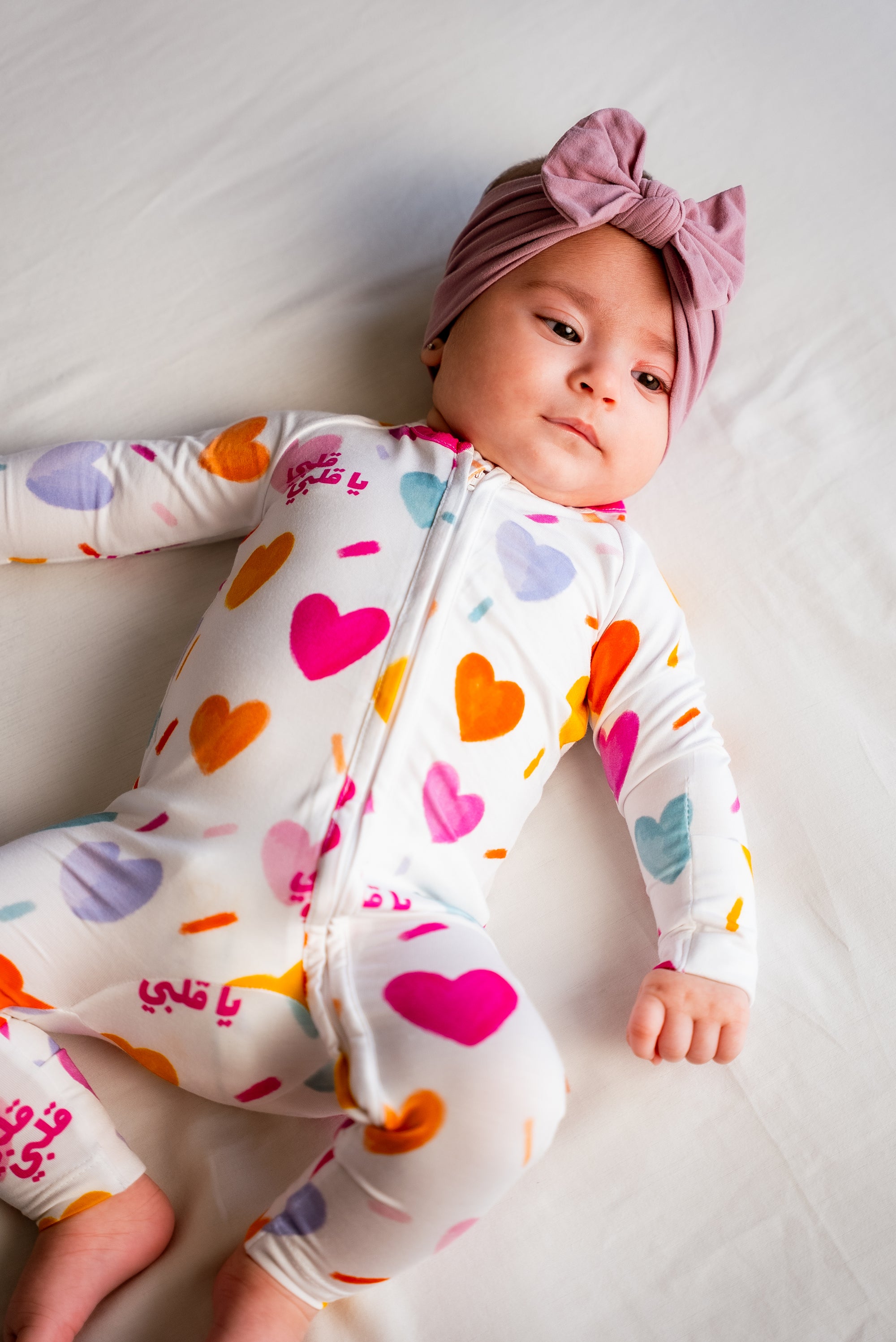 A baby wearing our Albi Smart Baby Pyjama, looking cozy and adorable in the colorful heart-print design.