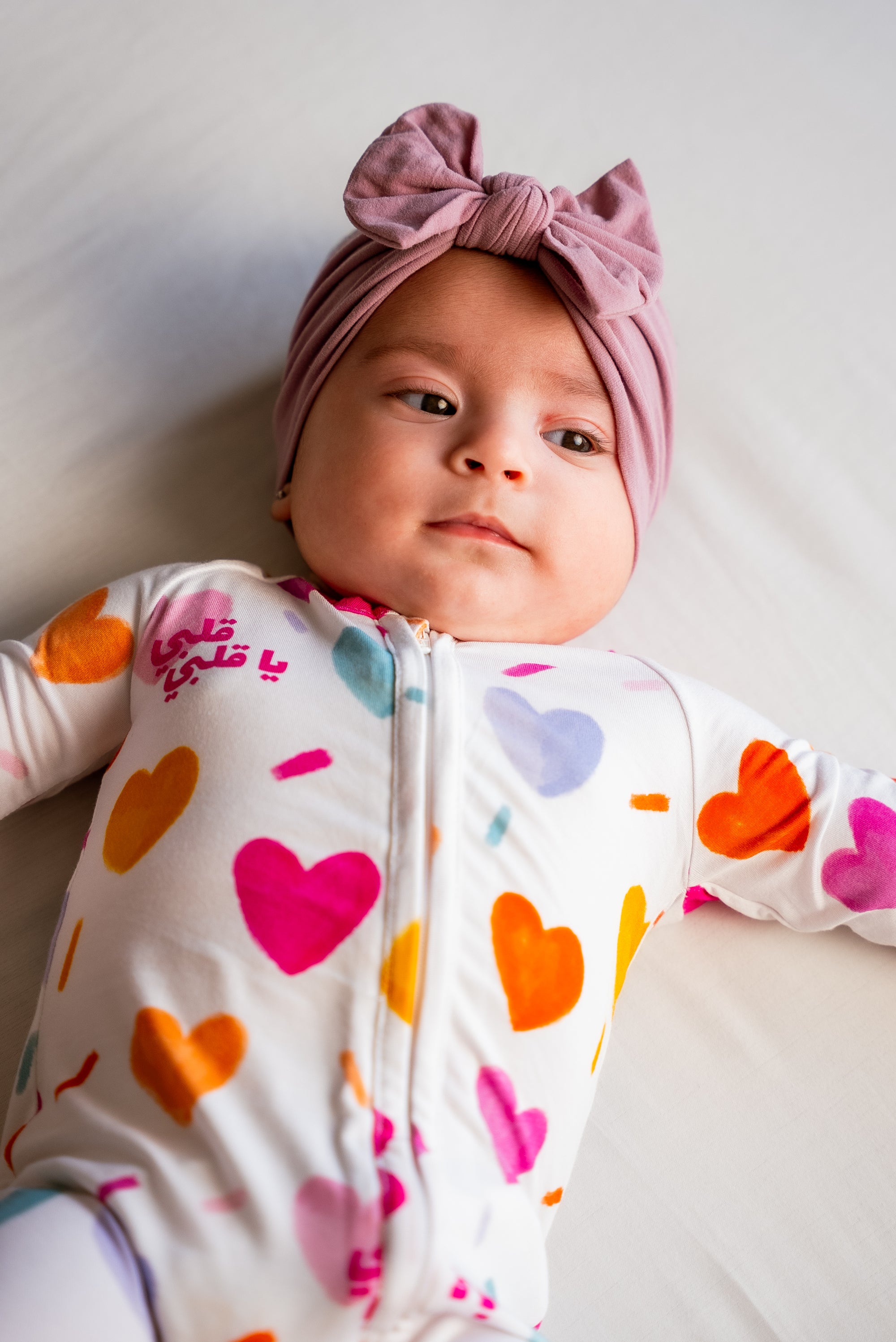 A baby wearing our Albi Smart Baby Pyjama, looking snug and sweet in the vibrant heart-print design.
