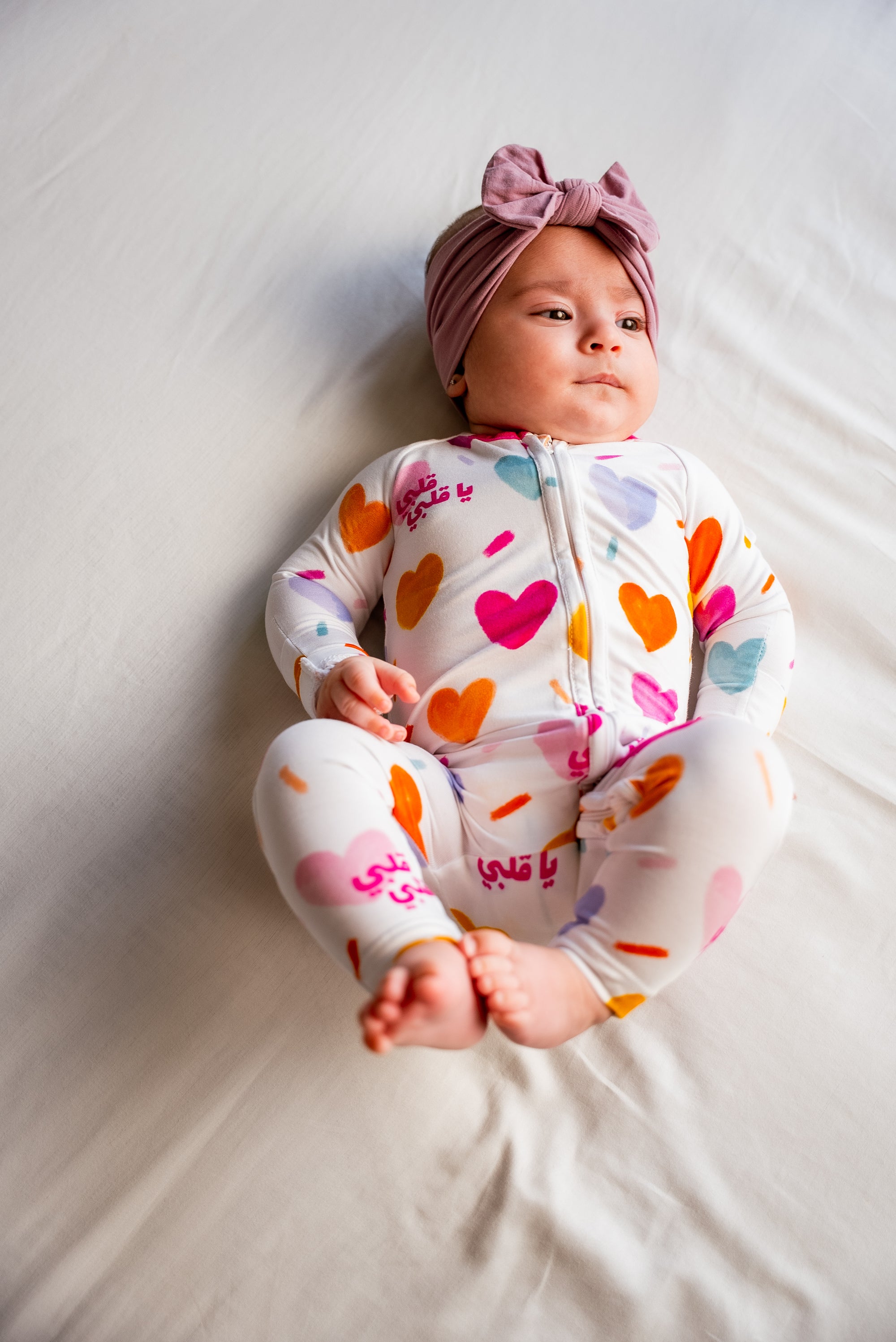 A baby wearing our Albi Smart Baby Pyjama, cozy and content in the playful heart-print design.