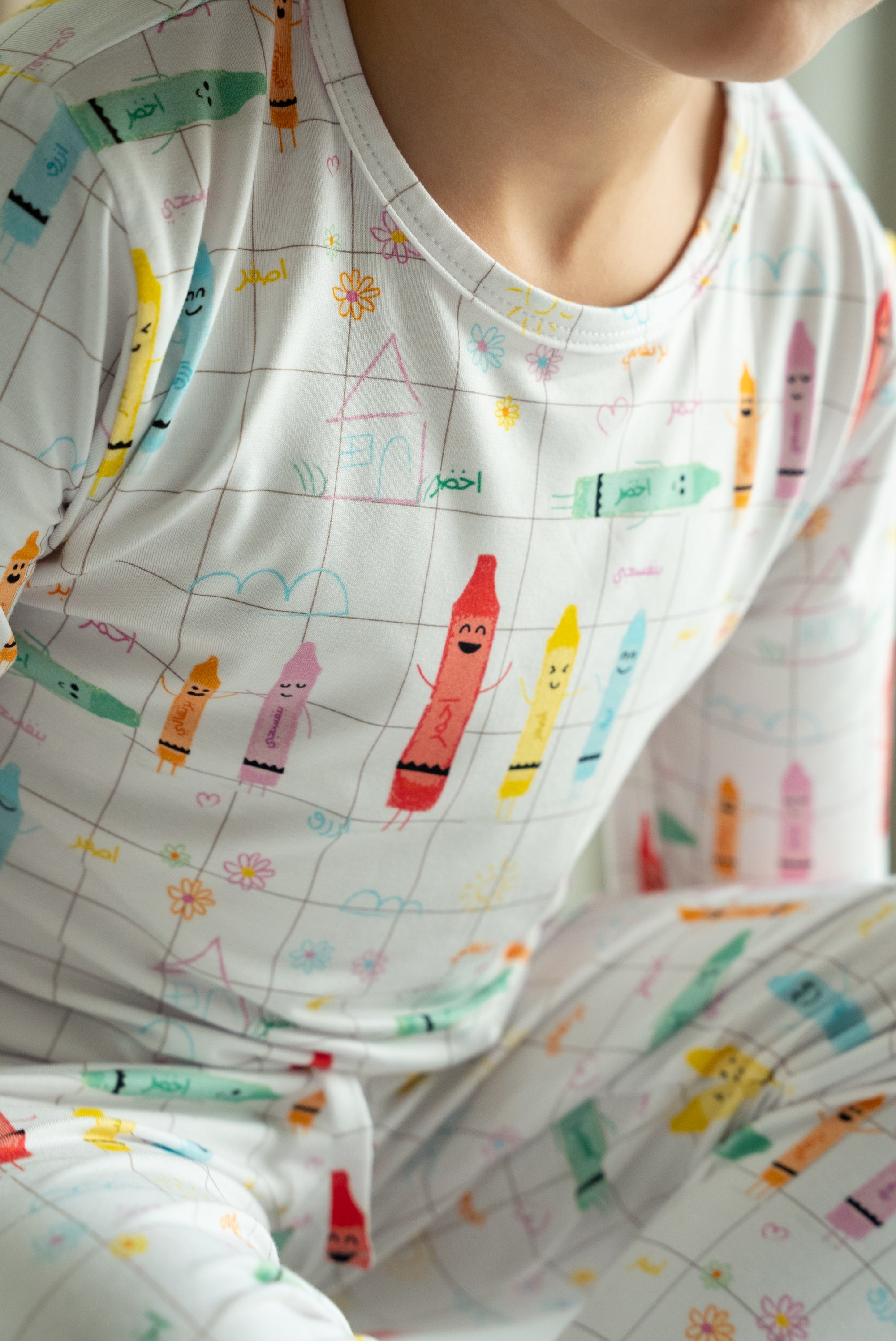 Close-up of a child wearing our Crayons Pyjama, showing the playful Arabic crayon designs and colourful doodle details.