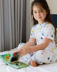 A girl wearing our Amara Short Sleeve Pyjama, enjoying story time in dreamy moon and star prints inspired by “Amara ya Amara.”
