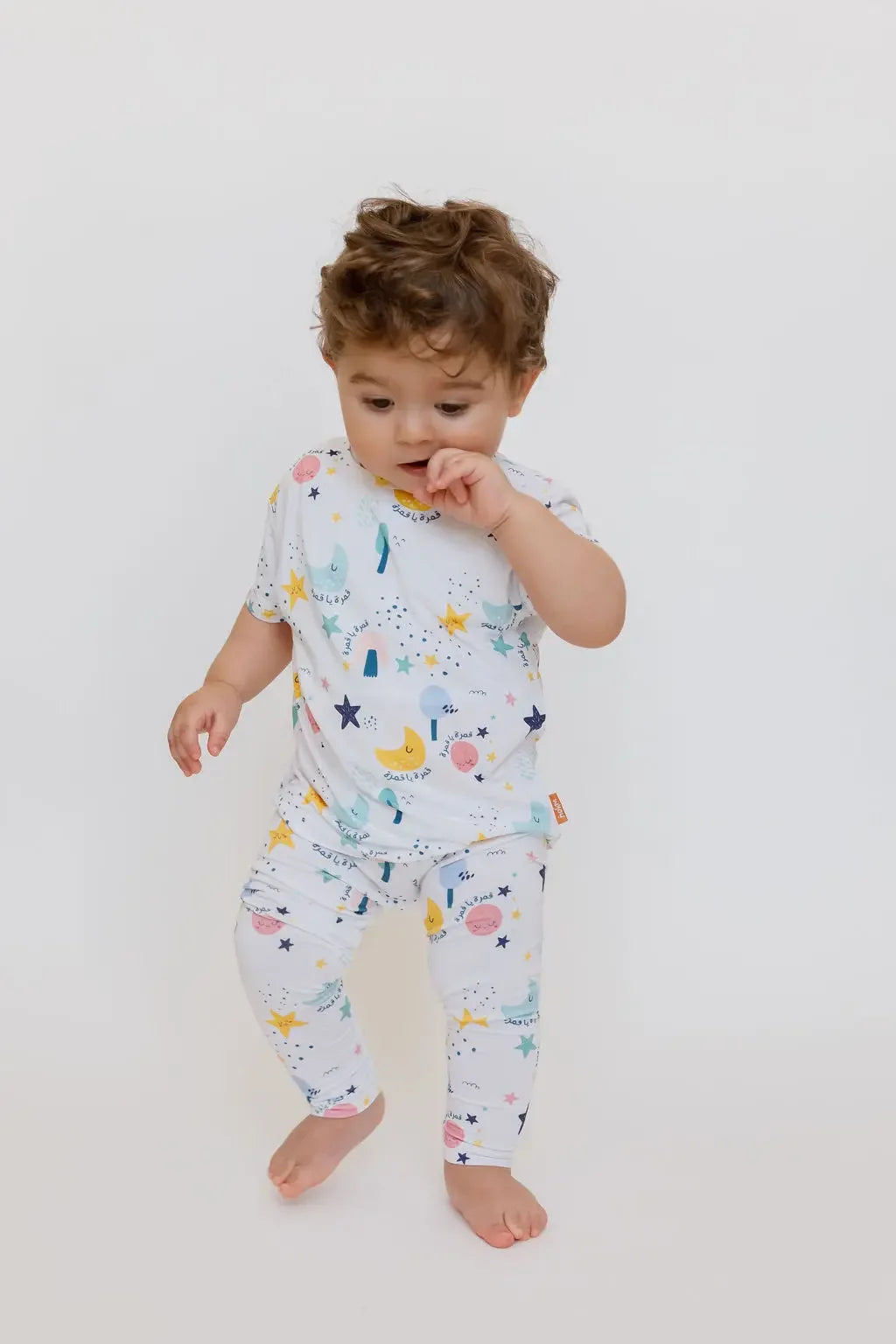 A baby wearing our Amara Short Sleeve Pyjama, exploring freely in soft bamboo fabric and whimsical moon-and-star prints.
