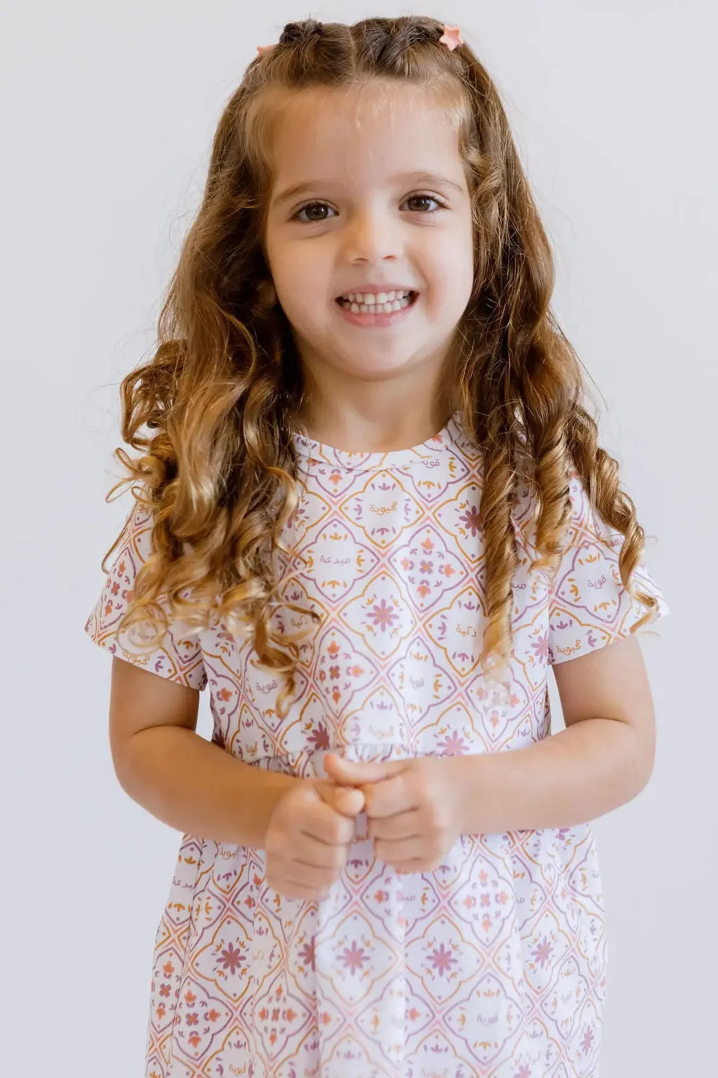 A cheerful girl smiling brightly while wearing our Arabesque Dress, adorned with elegant geometric patterns inspired by classical art.