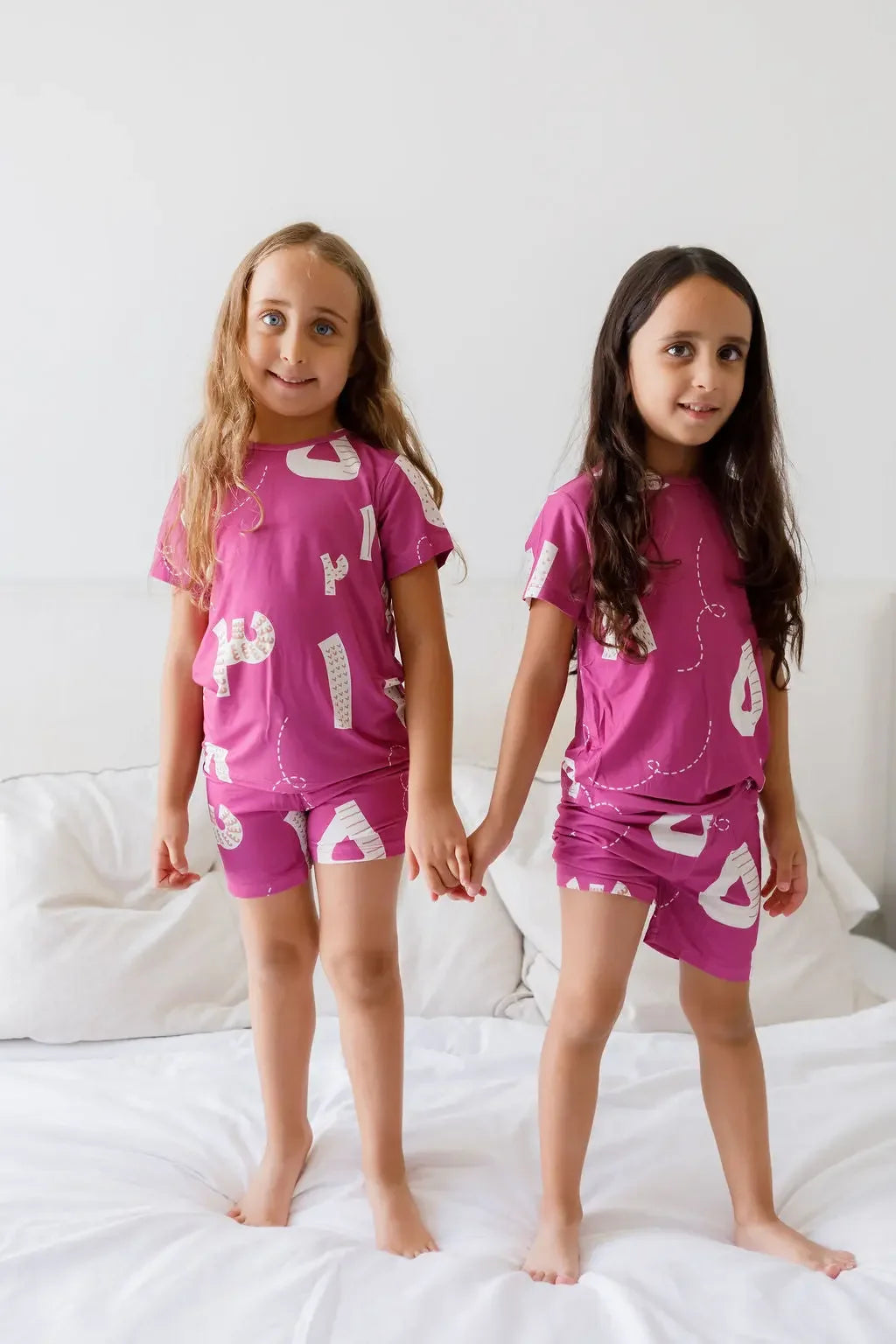 Two kids wearing our Arqam Short Sleeve Pyjama, featuring playful Arabic numbers on vibrant magenta bamboo fabric — comfy, breathable, and full of character.