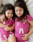 Sisters sharing cuddles in our Arqam Short Sleeve Pyjama, featuring playful Arabic numbers on soft, breathable bamboo fabric for cozy, matching moments.