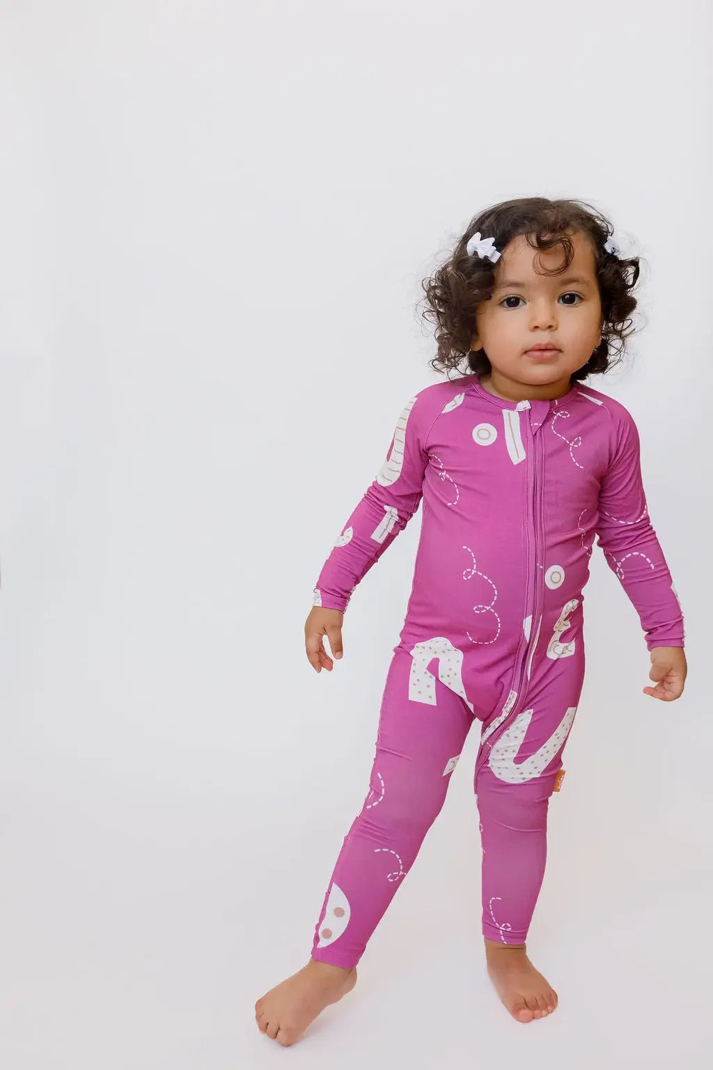 A curious little girl standing confidently while wearing our Arqam Smart Baby Pyjama, featuring bold Arabic numbers in a playful magenta print.