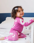 A happy girl giggling on the bed while wearing our Arqam Smart Baby Pyjama, covered in fun Arabic numbers for playful learning.