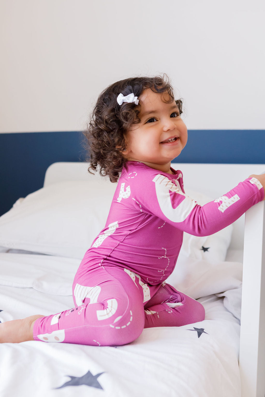 A happy girl giggling on the bed while wearing our Arqam Smart Baby Pyjama, covered in fun Arabic numbers for playful learning.