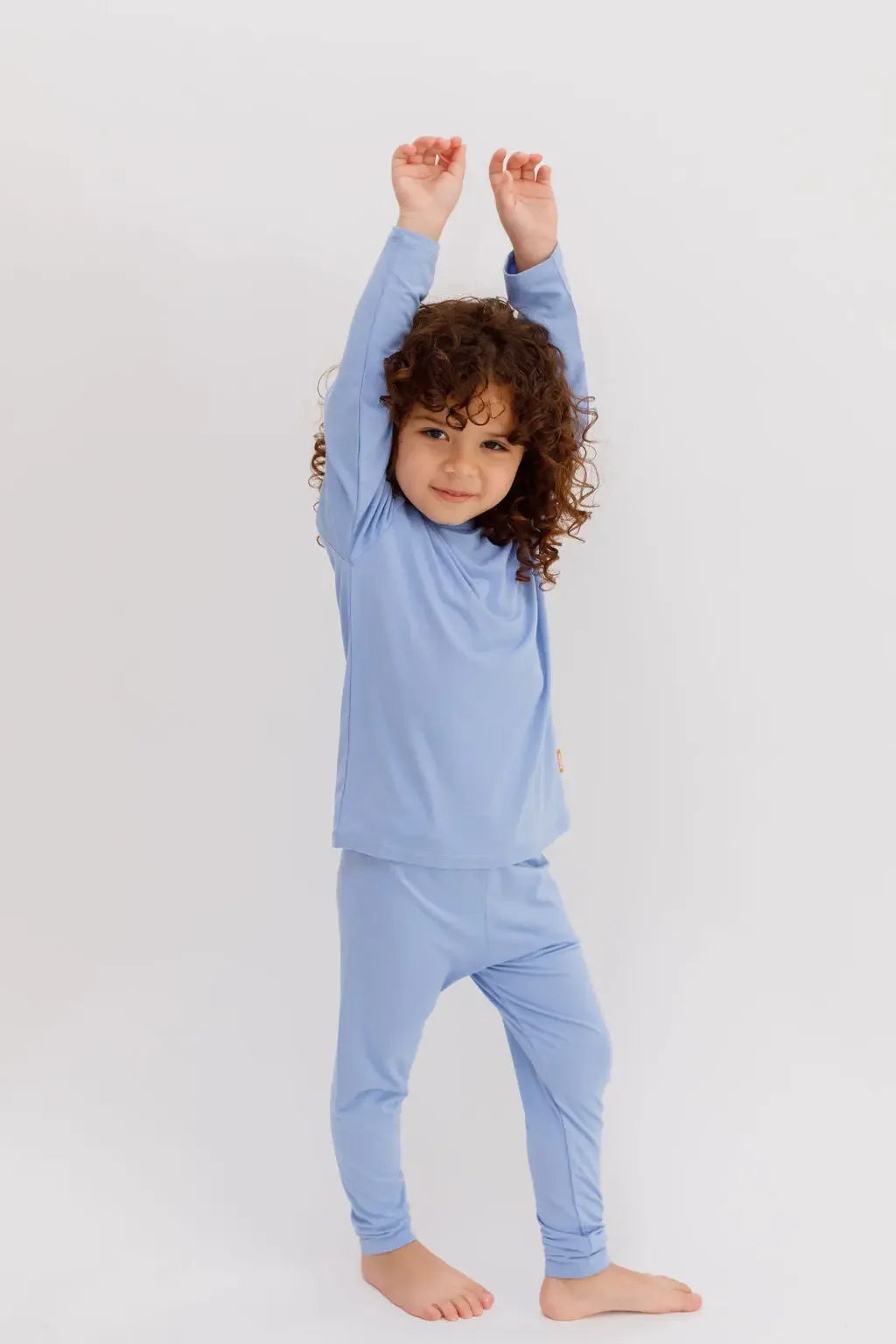 A playful child stretching in our Bahry Long Sleeve Kids Pyjama, made from ultra-soft bamboo fabric in a calming blue shade.