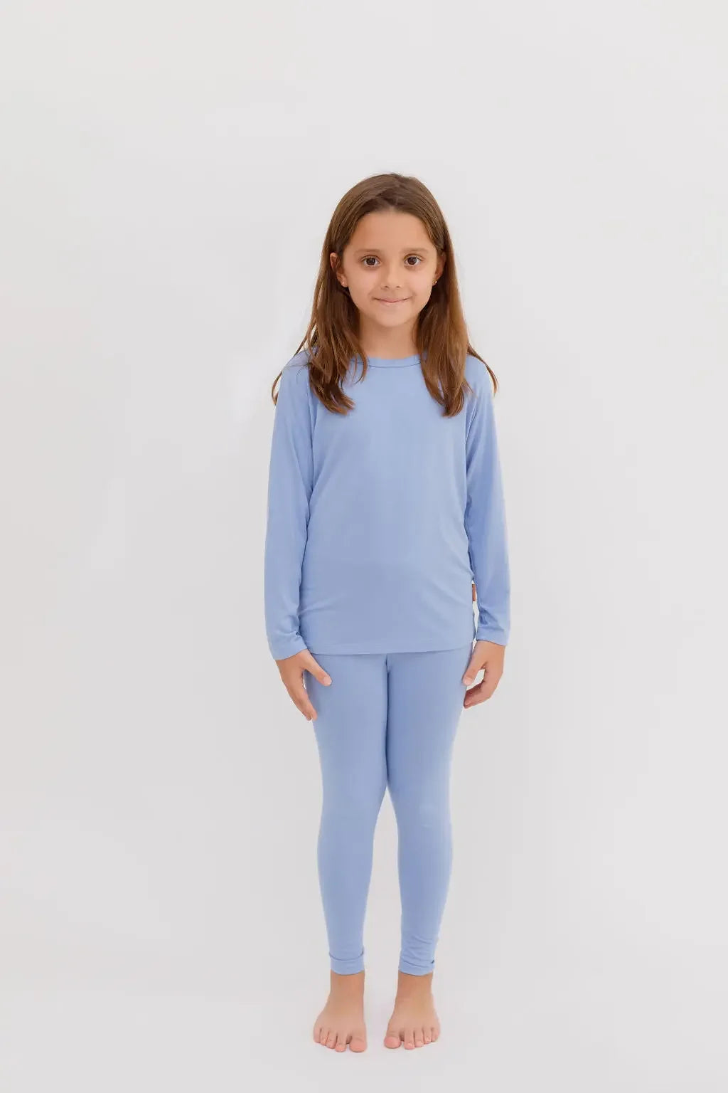 A smiling girl standing in our Bahry Long Sleeve Kids Pyjama, crafted from soft, breathable bamboo fabric in a soothing blue tone.