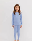 A smiling girl standing in our Bahry Long Sleeve Kids Pyjama, crafted from soft, breathable bamboo fabric in a soothing blue tone.