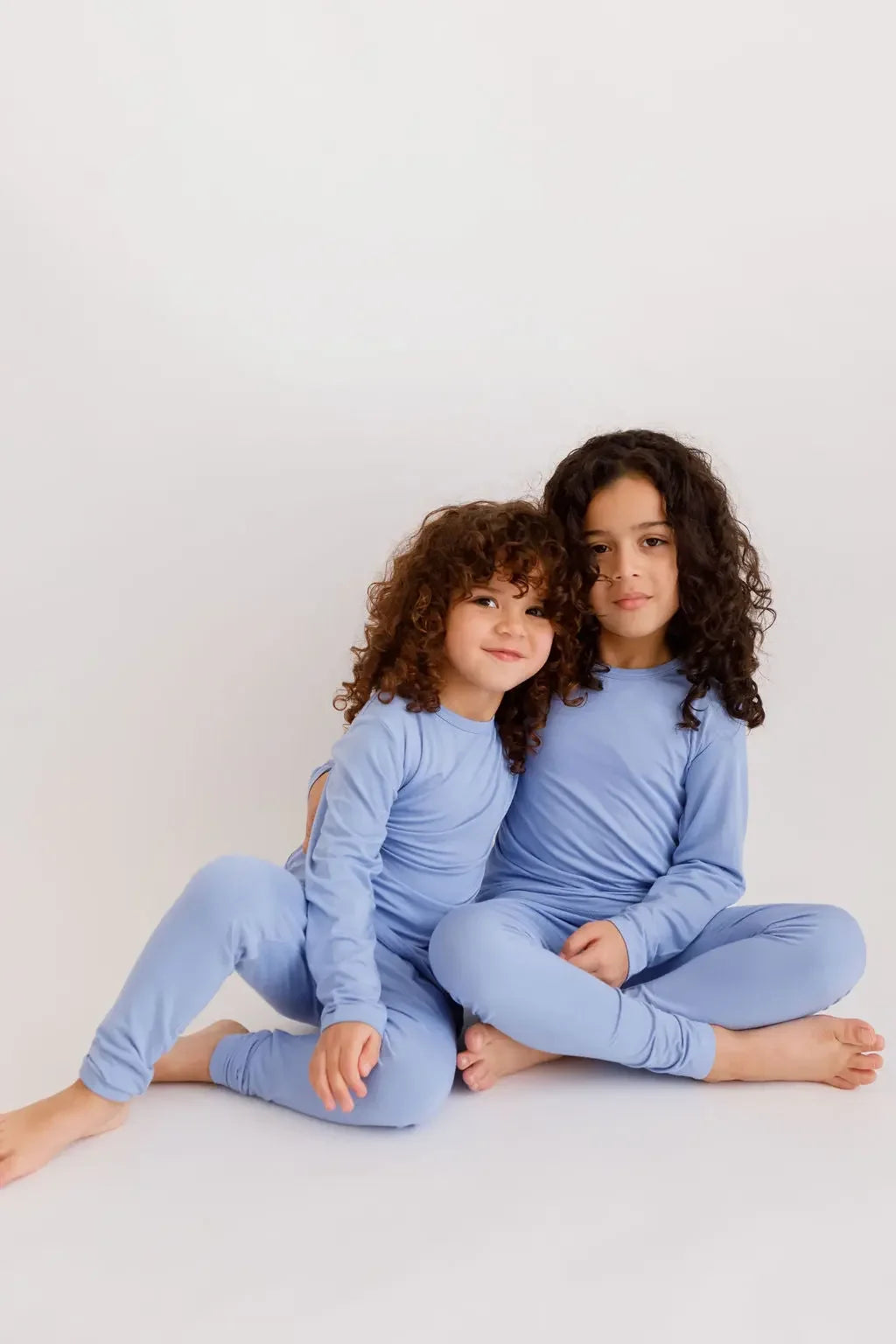 Two siblings sitting together in our Bahry Long Sleeve Kids Pyjamas, showcasing the cozy softness and calming blue tone of our bamboo fabric.