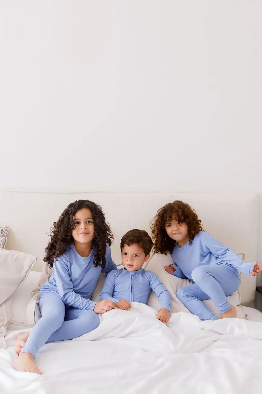 Three siblings sitting together on a cozy bed, all dressed in our Bahry Long Sleeve Kids Pyjamas, enjoying comfort in matching bamboo softness.