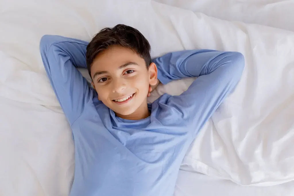 A smiling boy lying back on a soft bed in our Bahry Long Sleeve Kids Pyjama, enjoying the cozy comfort of bamboo fabric.