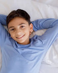 A smiling boy lying back on a soft bed in our Bahry Long Sleeve Kids Pyjama, enjoying the cozy comfort of bamboo fabric.