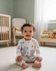 Baby sitting on a carpeted floor in a nursery with a crib and books in the background.