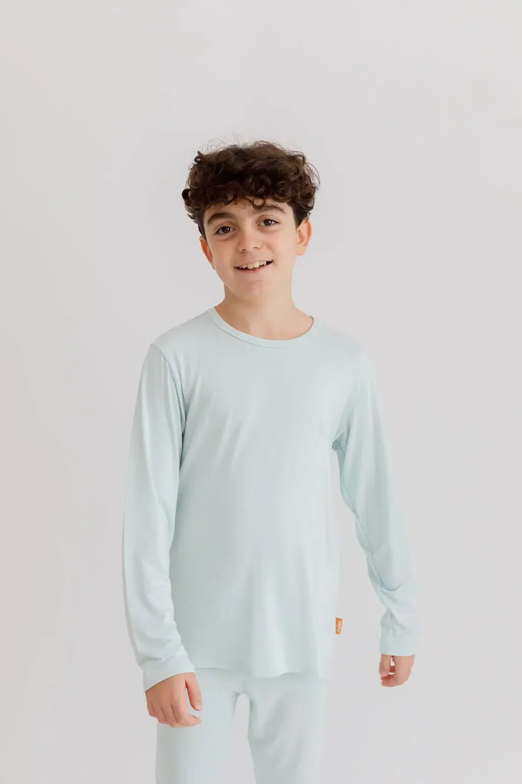 A young boy wearing the **Reef Pyjama** from the **Ramady & Reef Bundle**, a light seafoam-blue bamboo set designed for breathability, softness, and effortless comfort.
