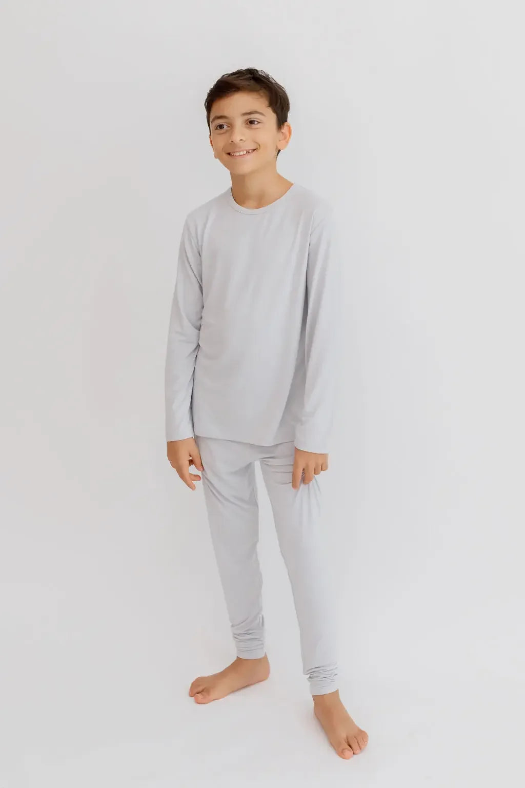 A young boy wearing the **Ramady Pyjama** from the **Ramady & Reef Bundle**, a soft light-gray long-sleeve set designed for all-night comfort and a relaxed fit.