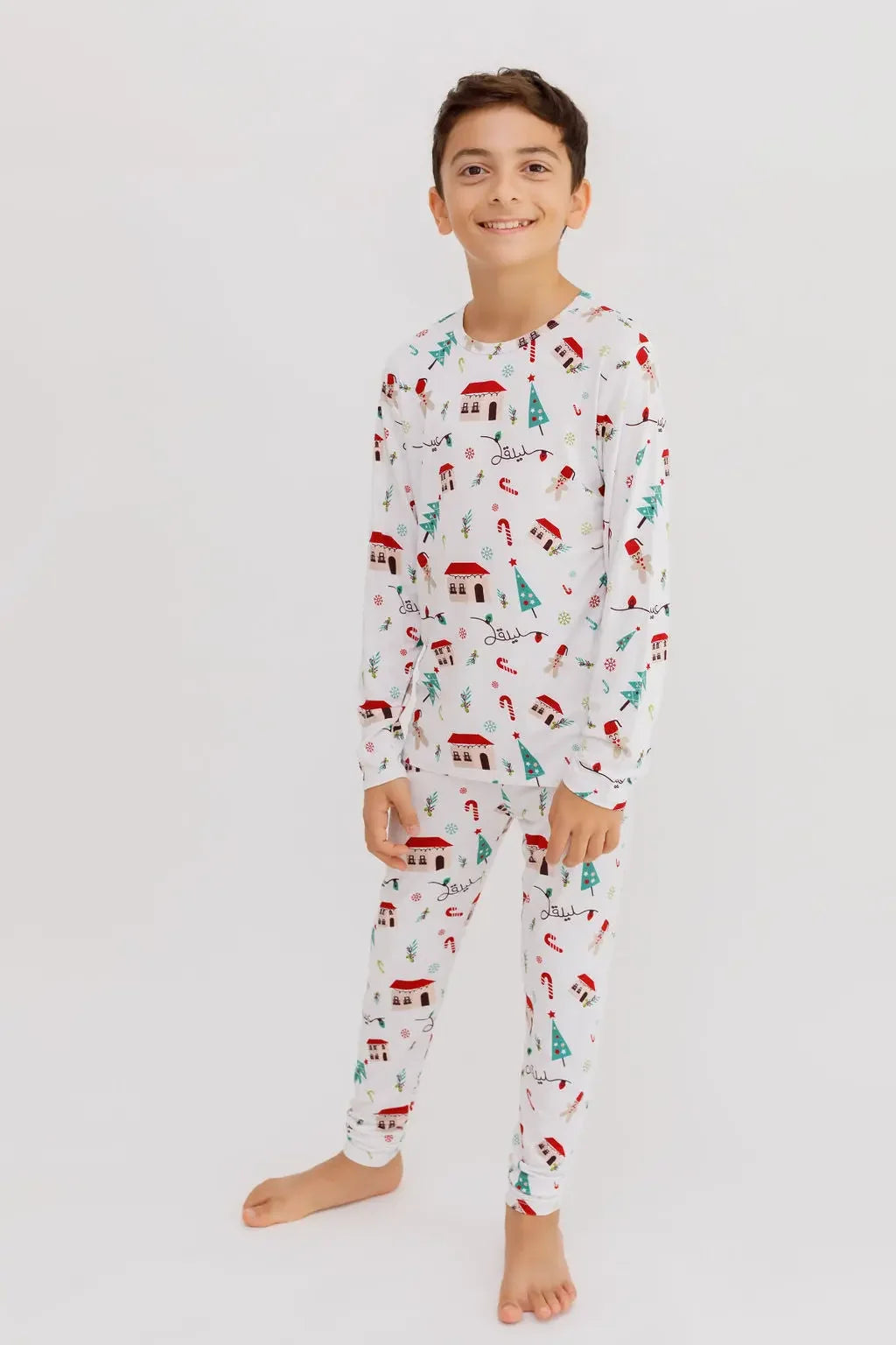 A smiling boy standing barefoot in our Christmas Long Sleeve Kids Pyjama, showcasing the festive Levant-inspired holiday print.