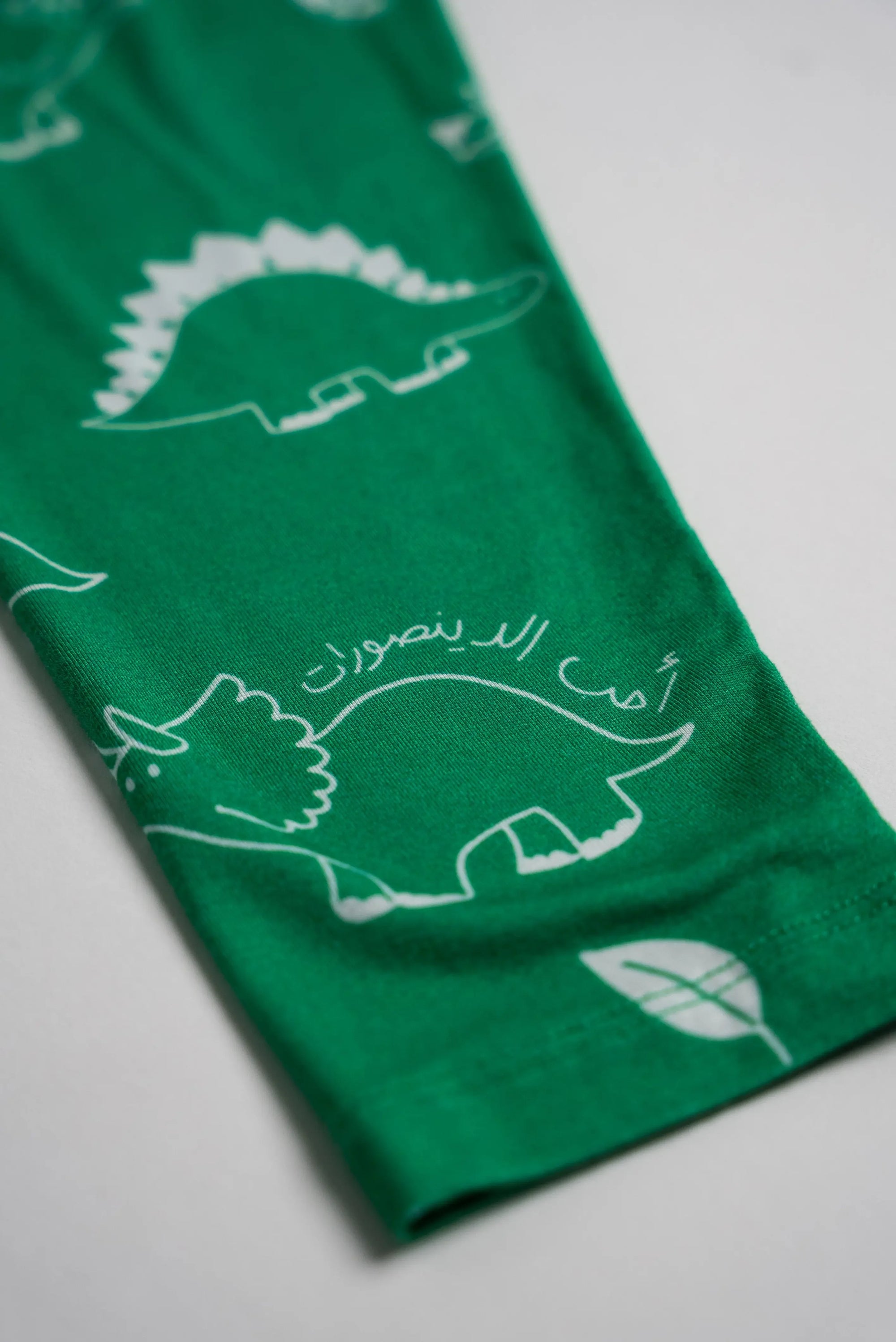 Close-up of our Dinosaur Pyjama sleeve, featuring playful white dinosaur illustrations and Arabic text on soft green bamboo fabric.