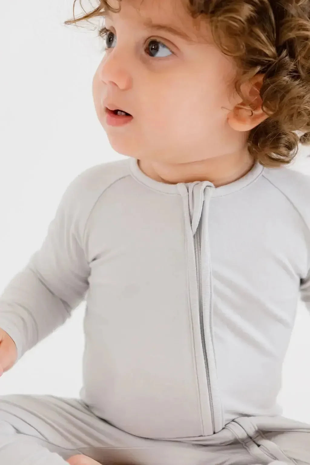 A baby wearing the **Ramady Pyjama** from the **Grow with Nohm: Gift Set**, a soft light-gray bamboo one-piece with a front zipper and gentle, snug fit for everyday comfort.