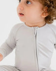 A baby wearing the **Ramady Pyjama** from the **Grow with Nohm: Gift Set**, a soft light-gray bamboo one-piece with a front zipper and gentle, snug fit for everyday comfort.