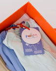 A close-up of the **Grow with Nohm: Gift Set**, showing neatly folded pastel baby pyjamas in an orange gift box with a branded Nohm tag.