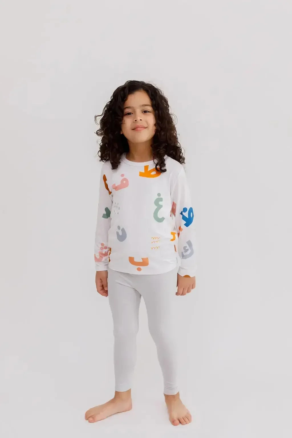A young child wearing the **Huroof Pyjama**, a white long-sleeve set decorated with colorful Arabic letters for a playful and cozy bedtime look.
