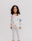 A young child wearing the **Huroof Pyjama**, a white long-sleeve set decorated with colorful Arabic letters for a playful and cozy bedtime look.

