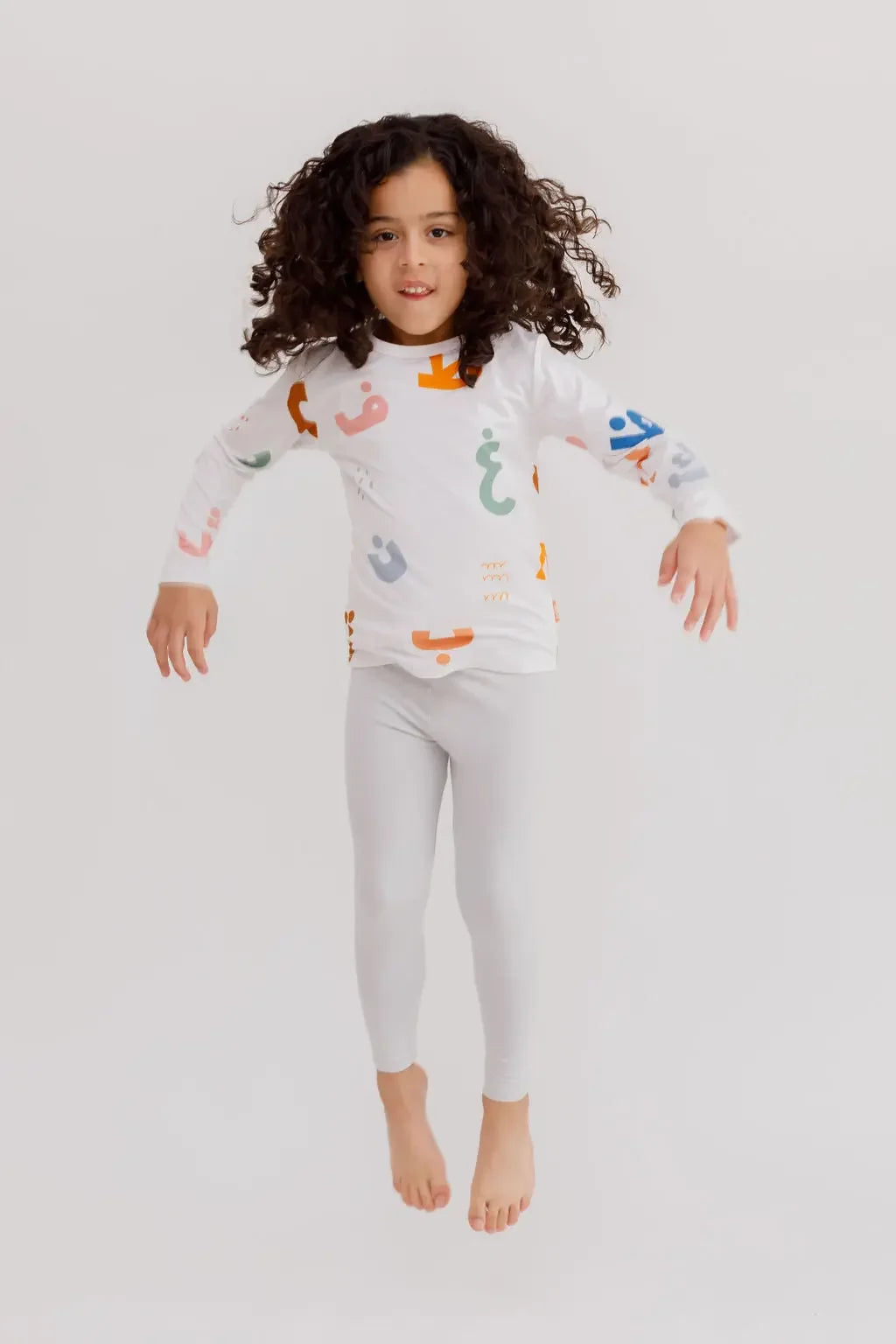 A joyful child jumping in our Huroof Long Sleeve Kids Pyjama, showcasing the playful Arabic calligraphy design in vibrant colors.