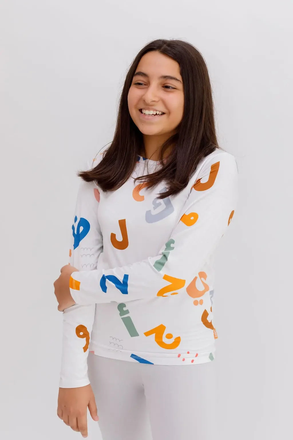 A smiling girl wearing our Huroof Long Sleeve Kids Pyjama, featuring bold and colorful Arabic calligraphy that celebrates heritage with a modern twist.