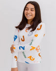 A smiling girl wearing our Huroof Long Sleeve Kids Pyjama, featuring bold and colorful Arabic calligraphy that celebrates heritage with a modern twist.