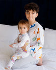 Two siblings sitting together on a bed, wearing our matching Huroof Long Sleeve Kids Pyjamas, celebrating comfort, connection, and Arabic-inspired design.
