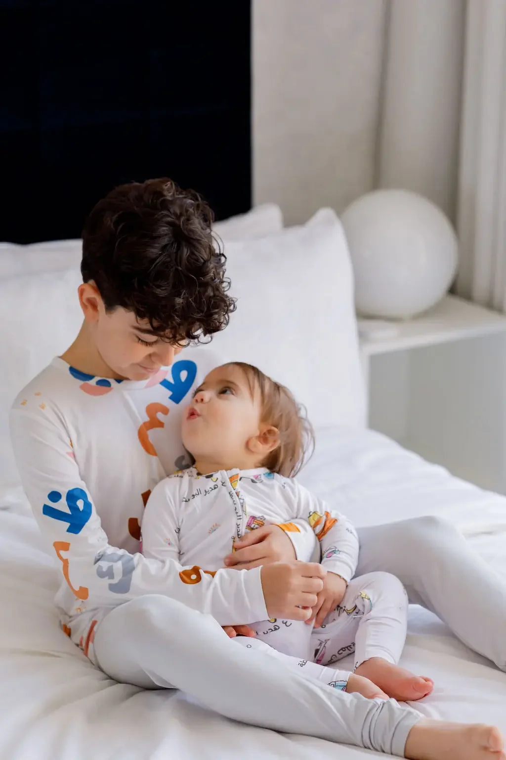 An older brother lovingly holding his baby sibling, both dressed in our matching Huroof Long Sleeve Kids Pyjamas, blending warmth, comfort, and cultural charm.