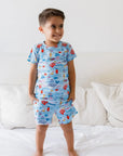 A happy boy standing on the bed while wearing our Kebr Al Baher short-sleeve set, featuring colorful sea creatures inspired by Fayrouz’s iconic song.
