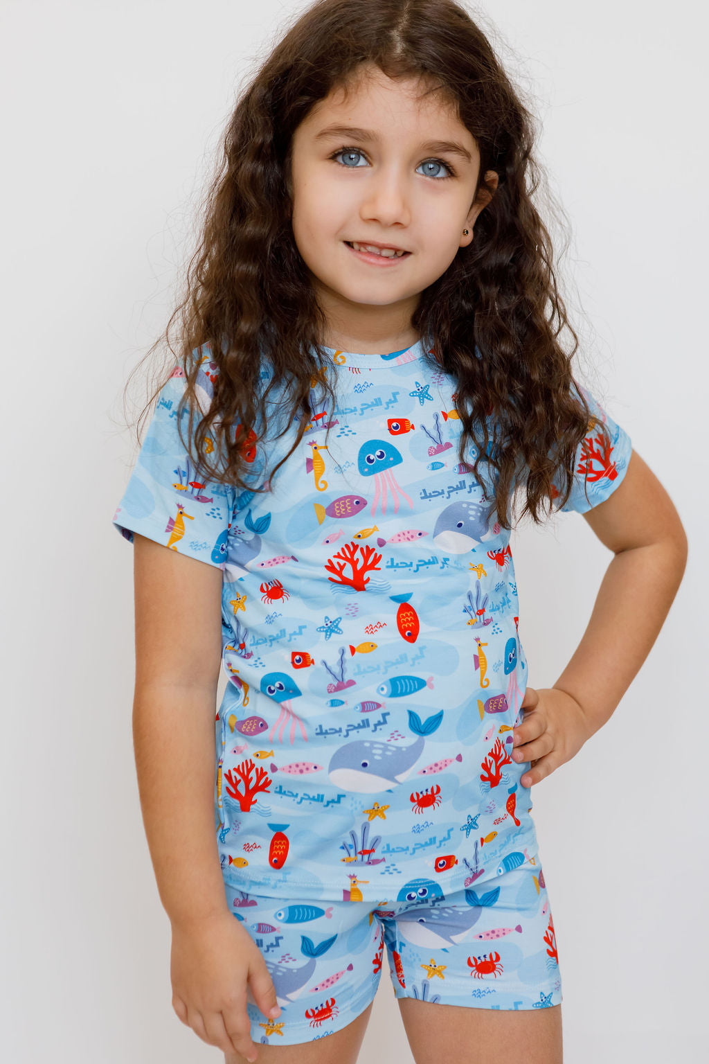 A confident girl posing with a smile while wearing our Kebr Al Baher short-sleeve set, featuring a playful underwater design inspired by Fayrouz’s song.