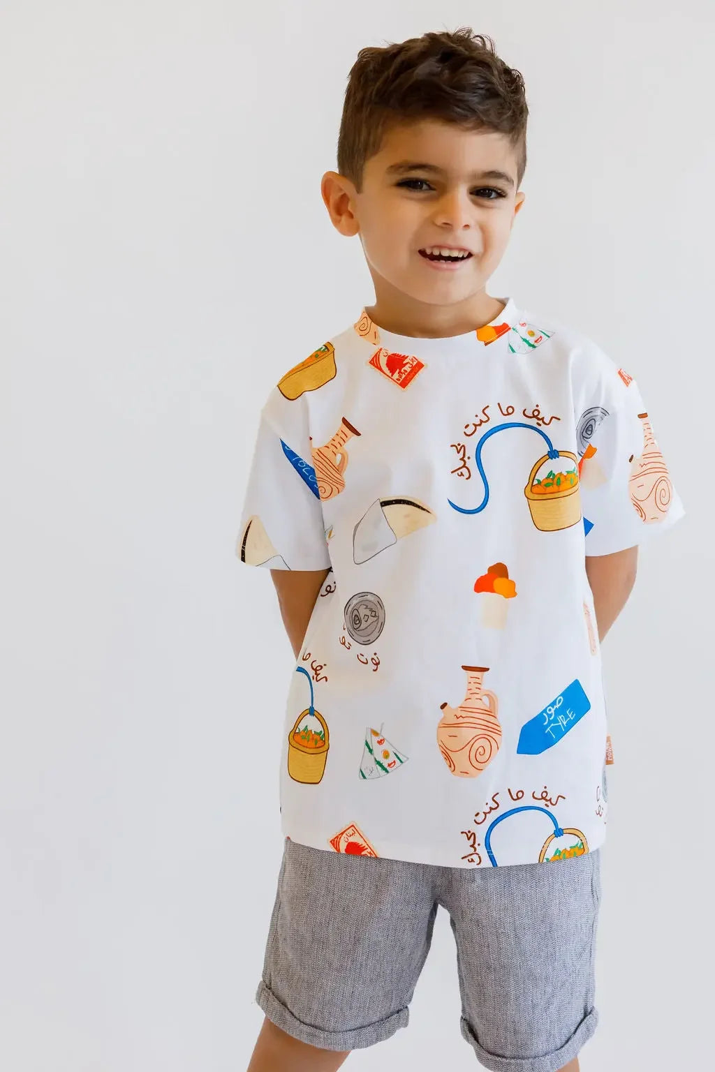 A cheerful boy standing with his hands in his pockets, wearing our Lebanon T-Shirt that celebrates the playful charm of Lebanese culture.