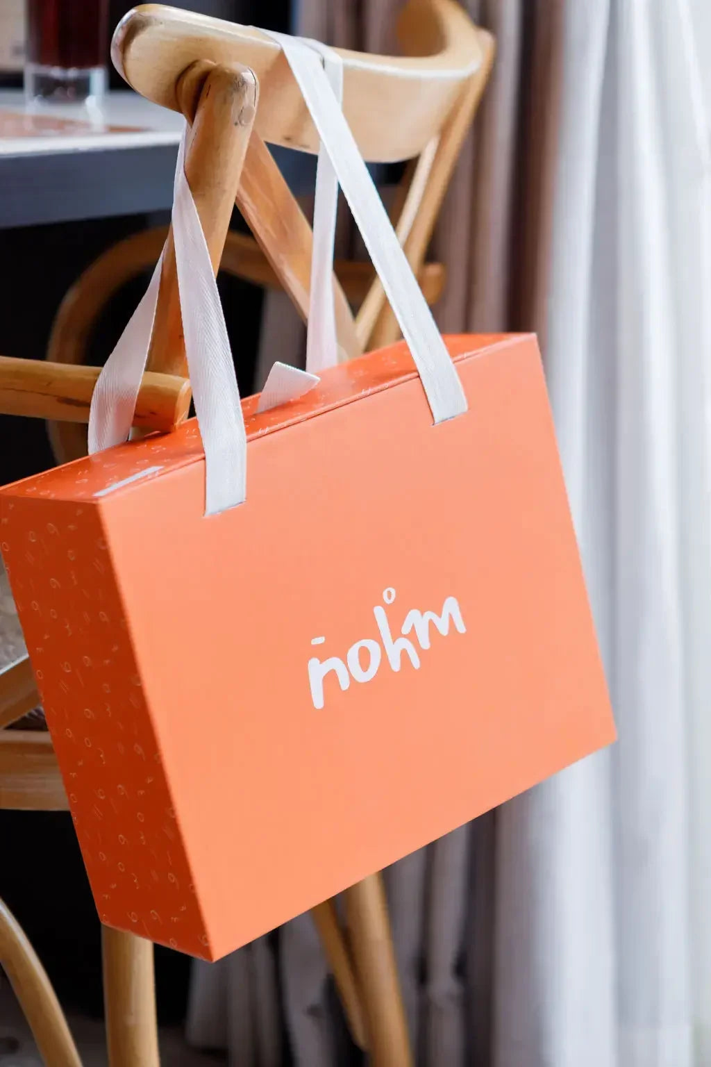A sleek orange Nohm Luxury Bedding Gift Set box hanging elegantly on a wooden chair, ready to be gifted.