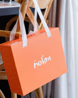 A sleek orange Nohm Luxury Bedding Gift Set box hanging elegantly on a wooden chair, ready to be gifted.