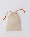 A soft beige Nohm pouch with orange drawstrings, designed to neatly hold the pieces of our Nohm Luxury Bedding Gift Set.