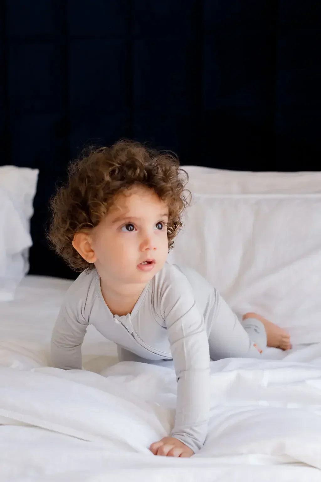 A curious toddler crawling on the bed while wearing our Ramady Pyjama, a soft and cozy solid grey set perfect for peaceful nights.

