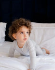 A curious toddler crawling on the bed while wearing our Ramady Pyjama, a soft and cozy solid grey set perfect for peaceful nights.
